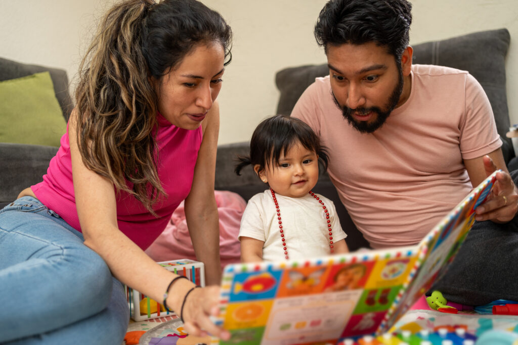 Mother and Father sitting on the ground reading book to baby daughter