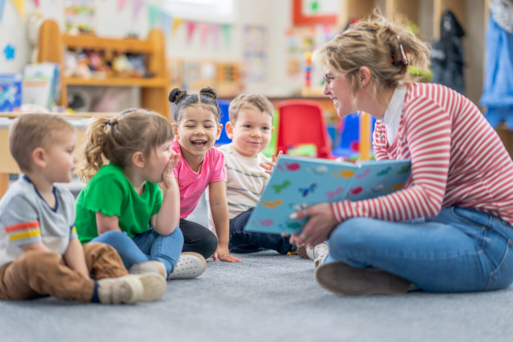 Teacher sitting on floor reading book to group of toddler-aged children